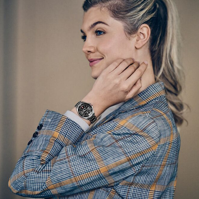 Woman wearing a plaid shirt and a watch, smiling and adjusting her hair.